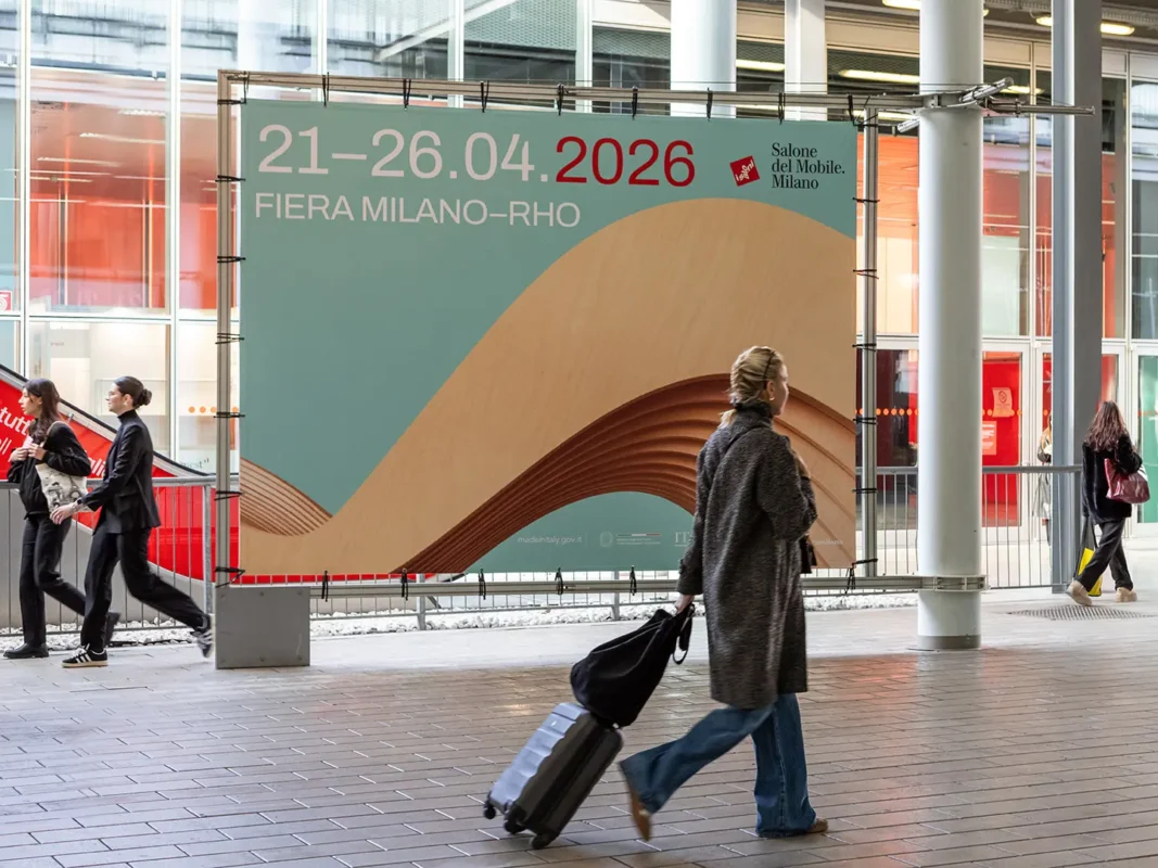 large billboard announcing salone del mobile milano 2026 at fiera milano rho with people walking by