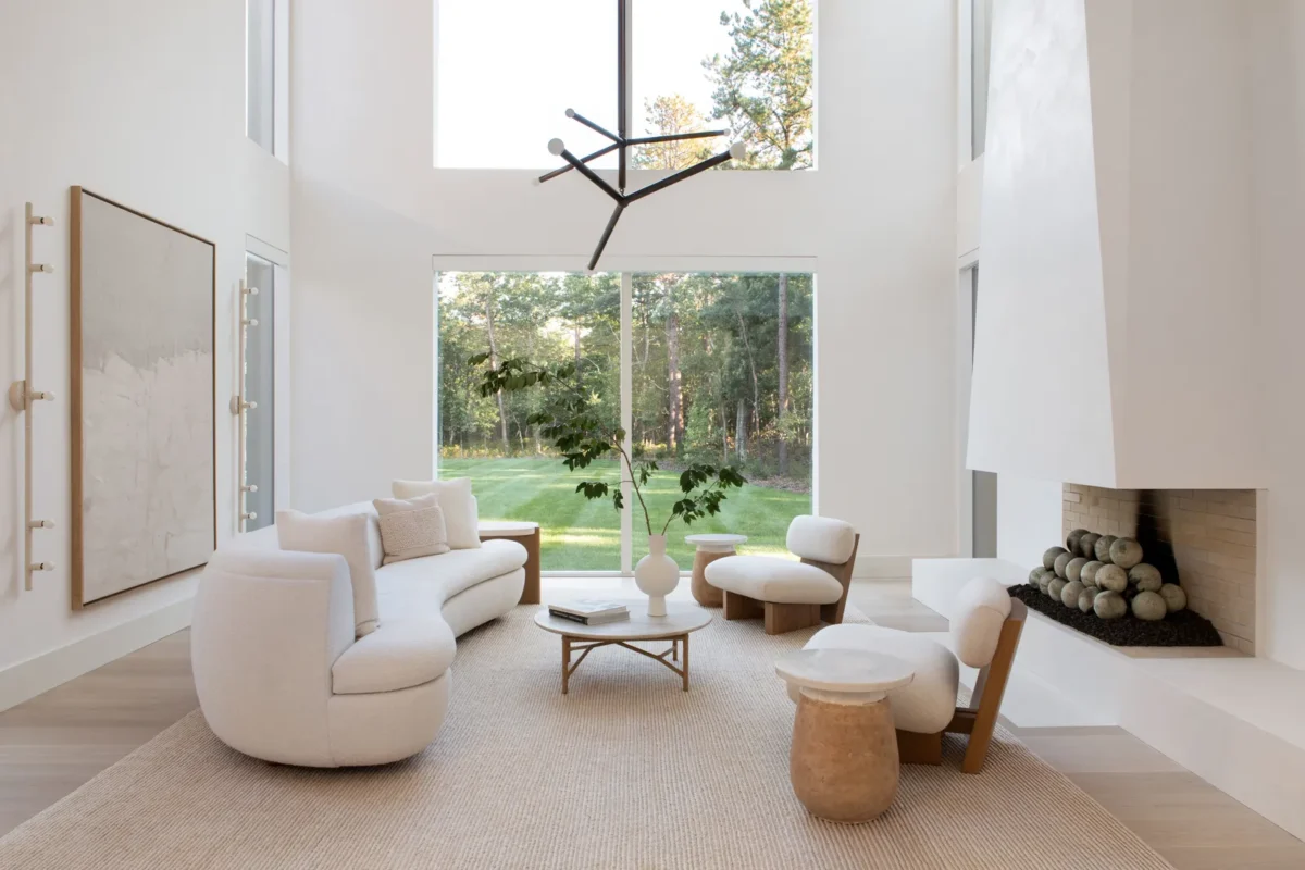 Minimalist white living room with modern furniture, large windows, and a sleek fireplace design.