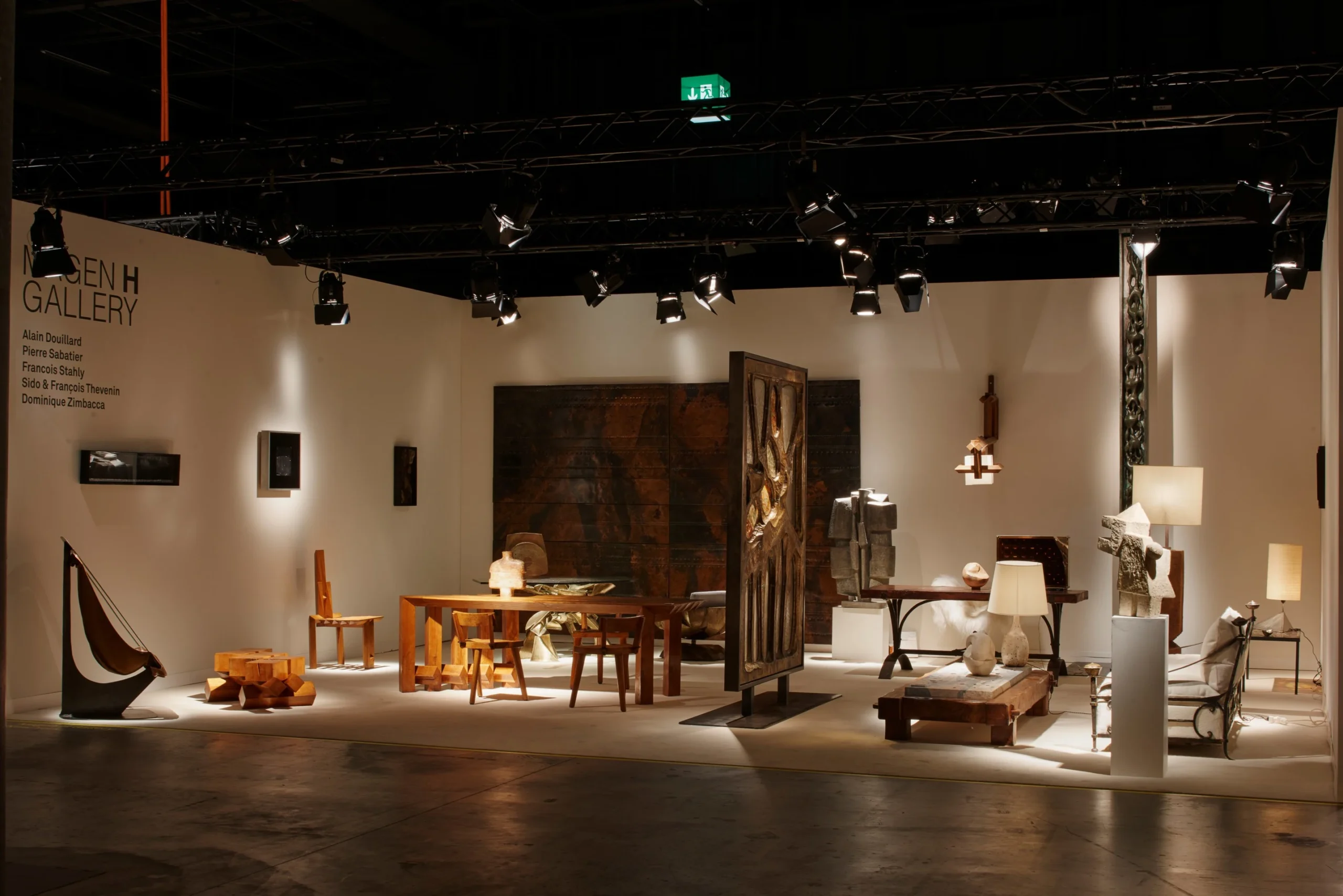 Contemporary design fair booth showcasing sculptural wooden furniture, lamps, and wall art under gallery lighting.
