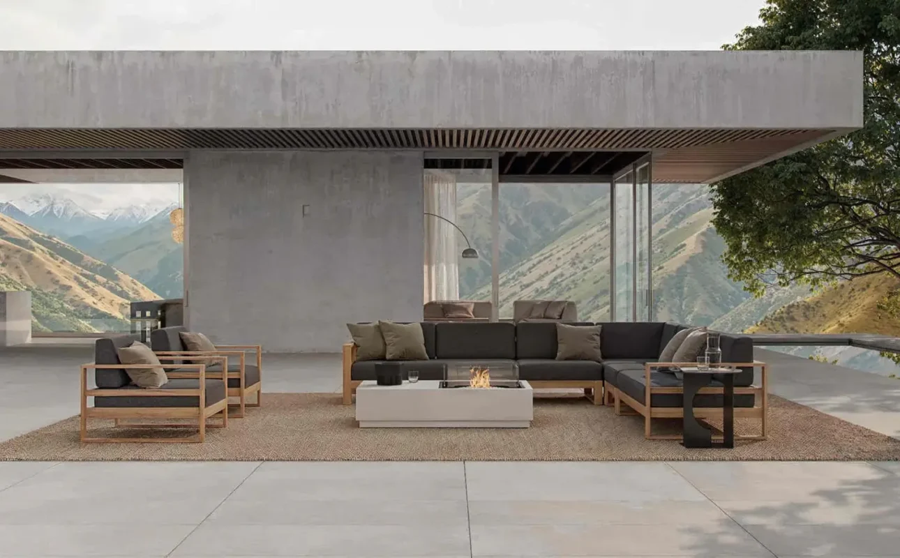 Modern outdoor living space with mountain views, minimalist concrete architecture, sectional sofa, and fire pit centerpiece.