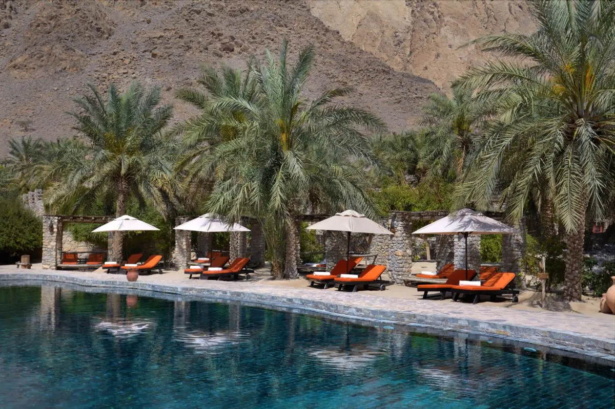 Palm-shaded poolside loungers and stone cabanas at Six Senses Zighy Bay in Oman.