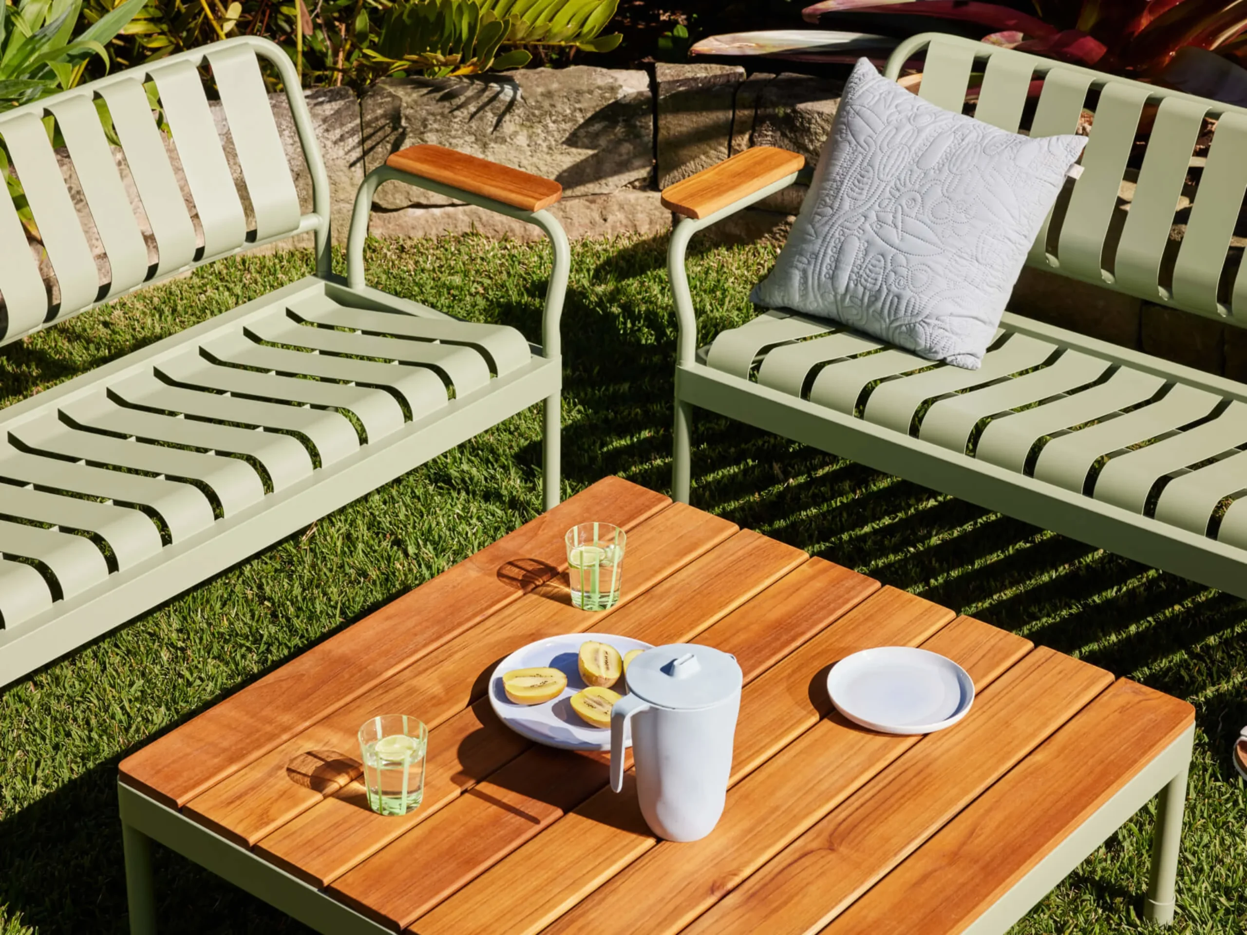Minimalist outdoor lounge furniture with green metal slatted chairs and a wooden table set for a casual summer drink.