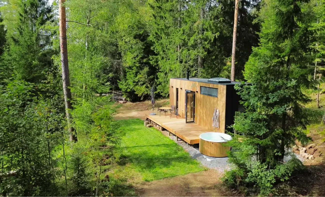 A modern wooden cabin with outdoor deck and hot tub nestled in a lush Scandinavian forest.
