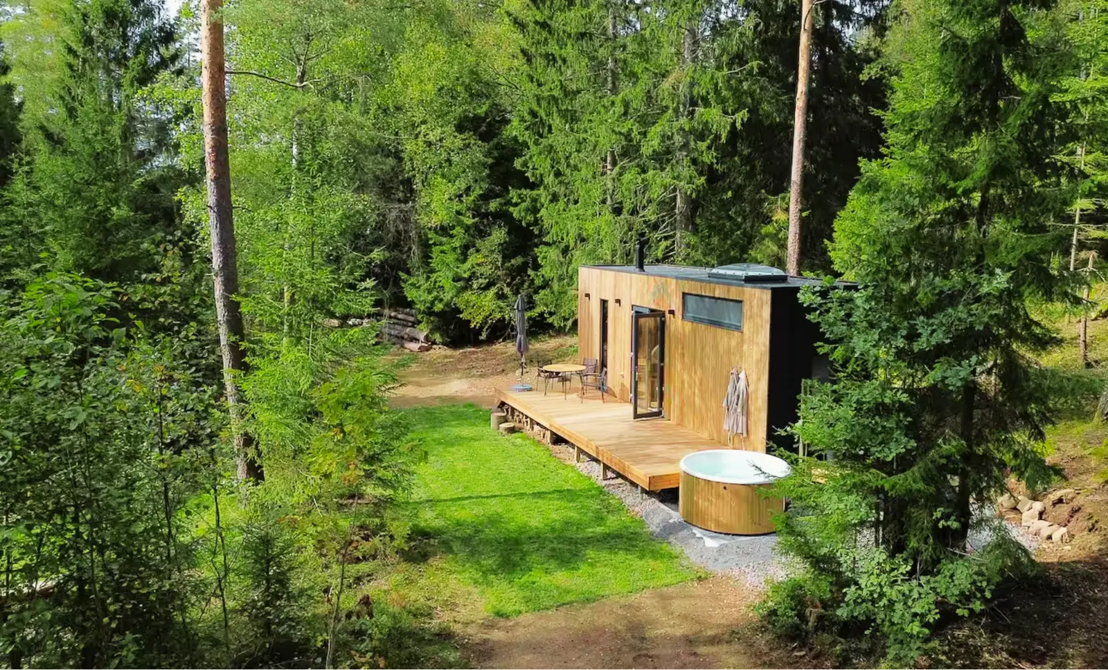 A modern wooden cabin with outdoor deck and hot tub nestled in a lush Scandinavian forest.