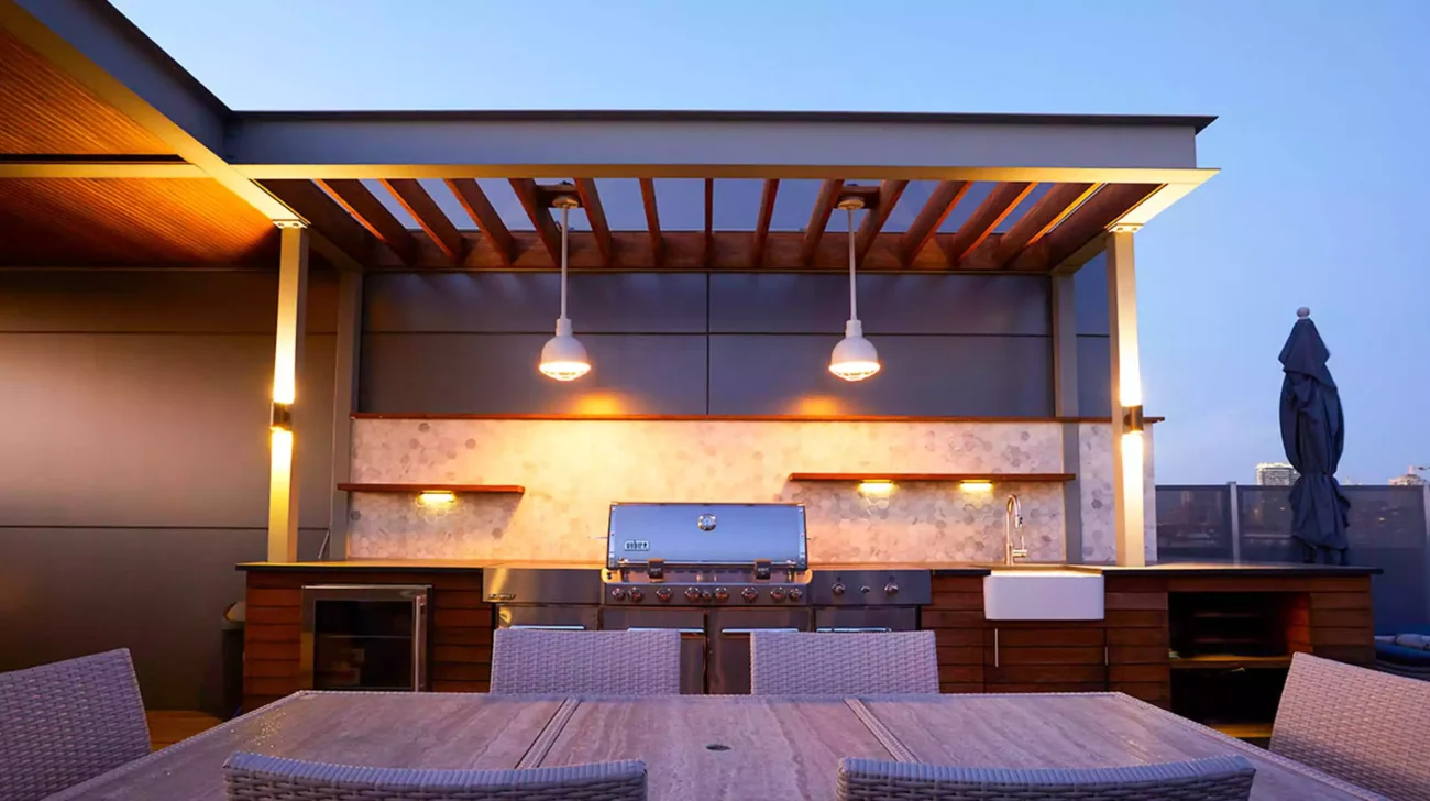 modern rooftop outdoor kitchen with grill, wooden cabinetry, and pendant lights.