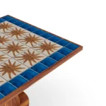 Close-up of the Vedrà tabletop, highlighting the textured relief tiles, the vibrant blue glaze, and the fine craftsmanship of the iroko frame.