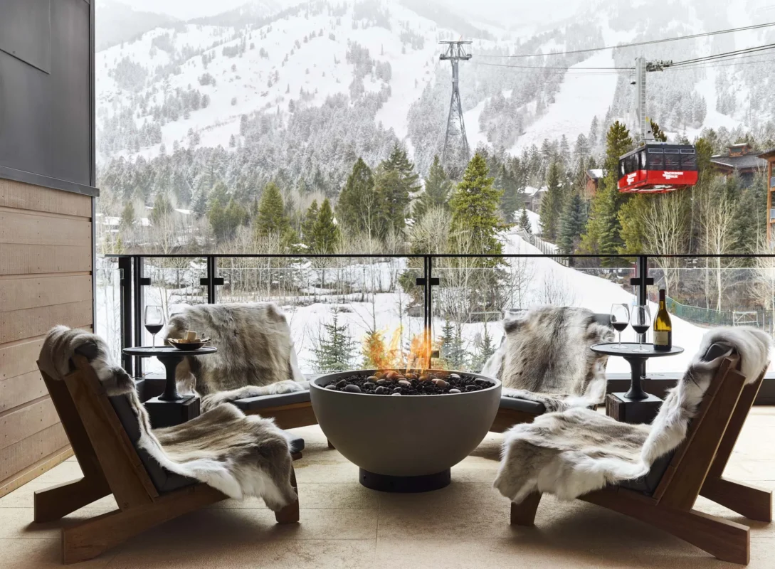 Contemporary fire bowl with glowing flames on a mountain-view balcony, surrounded by fur-draped lounge chairs.