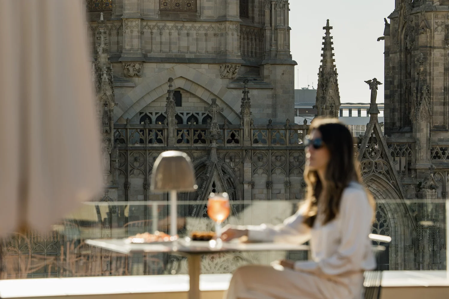 Luxury rooftop terrace with a woman enjoying a cocktail overlooking Gothic cathedral architecture: outdoor furniture inspiration