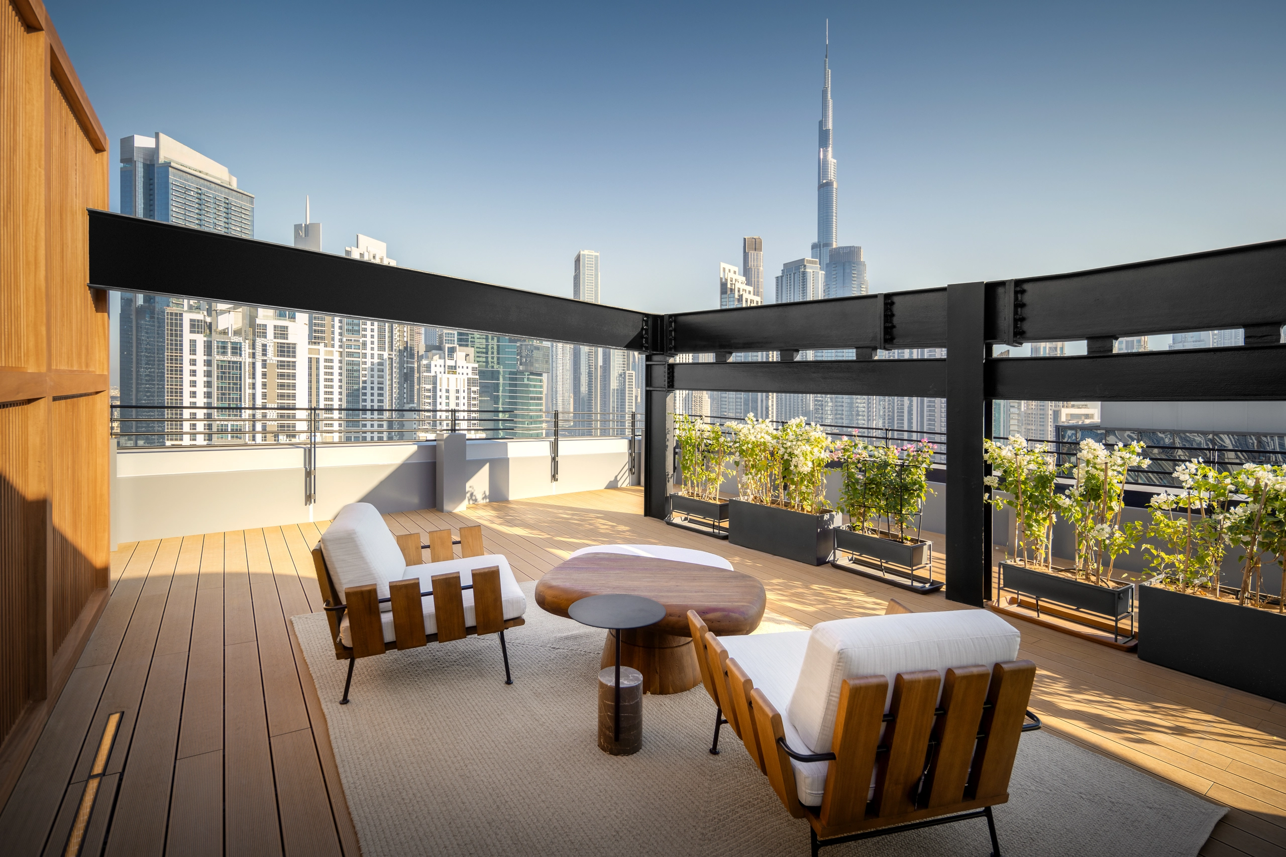 Luxury rooftop terrace in Dubai with modern wooden lounge chairs, sculptural coffee tables, and skyline views of Burj Khalifa.