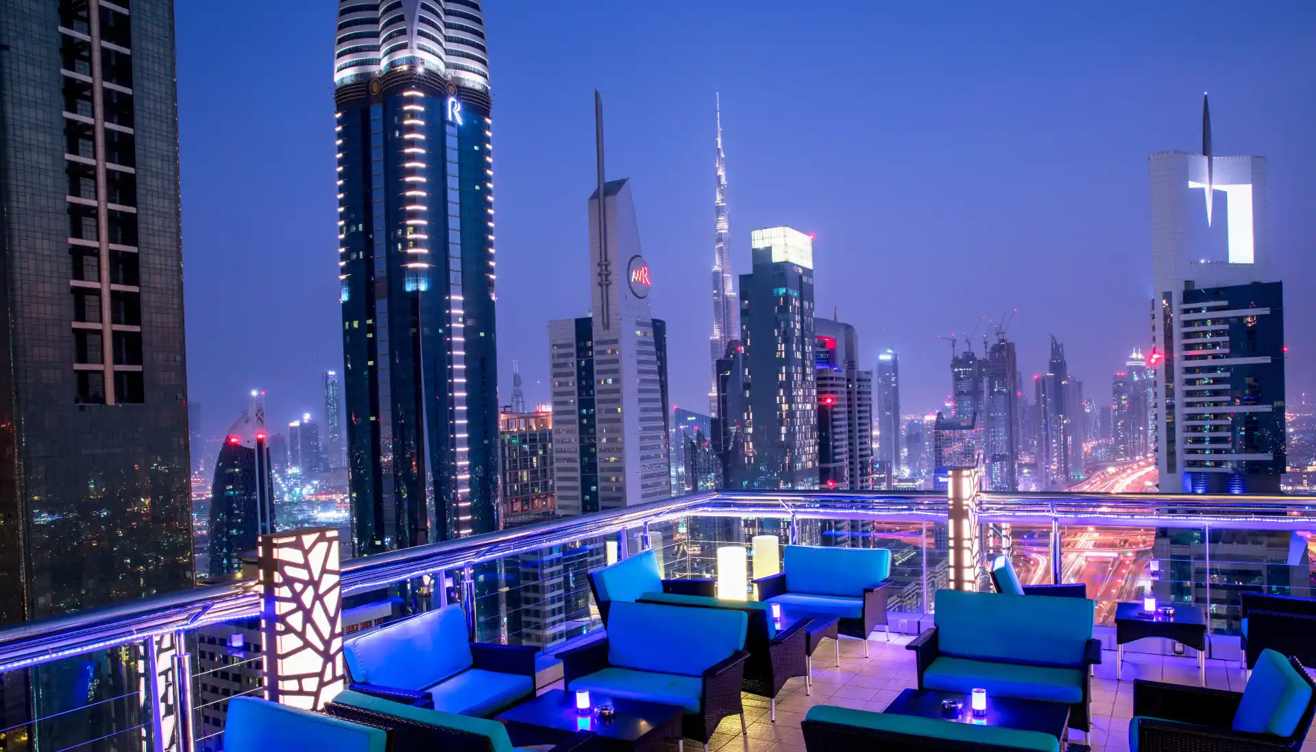 Dubai rooftop lounge with blue seating and panoramic skyline views including Burj Khalifa at night.
