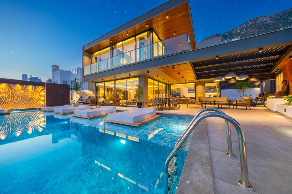 Modern villa with glass walls, floating sun loungers, and illuminated pool deck in a luxury resort-style setting.