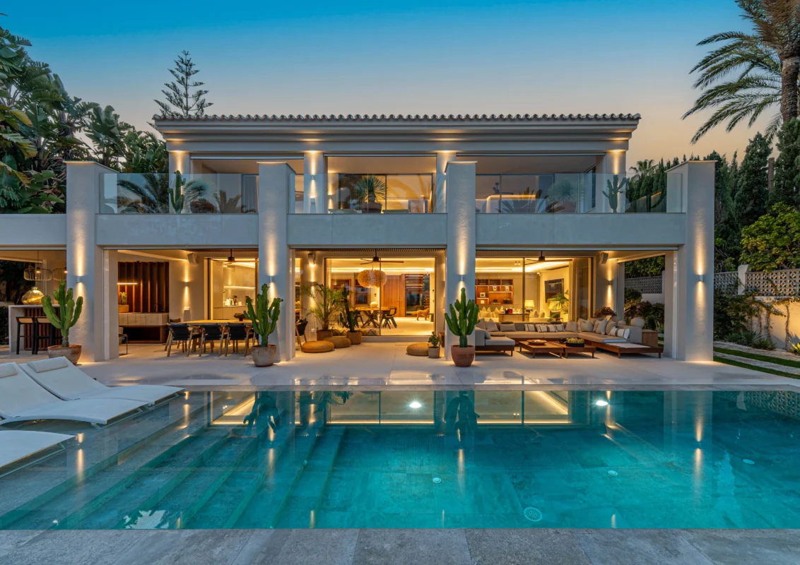 Contemporary Mediterranean-style villa with expansive terraces, illuminated columns, and private pool at sunset.