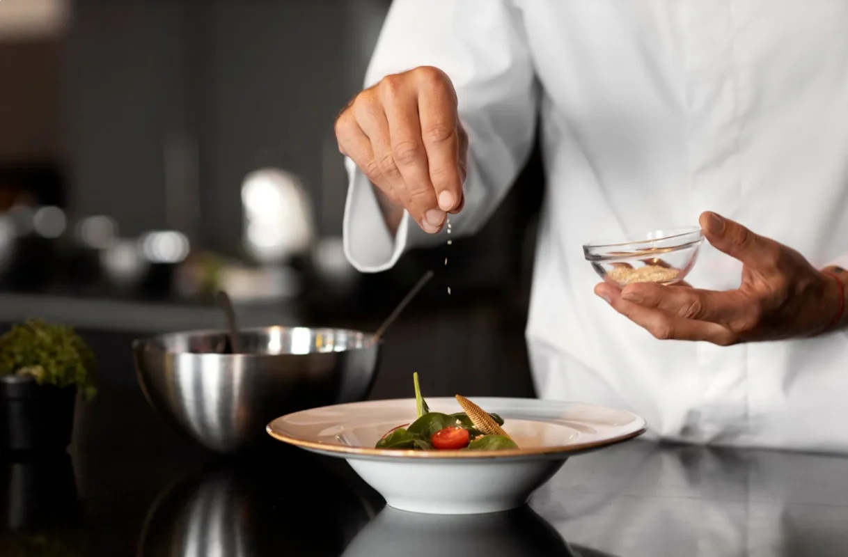 Private chef adding final seasoning to a gourmet dish in a luxury kitchen.