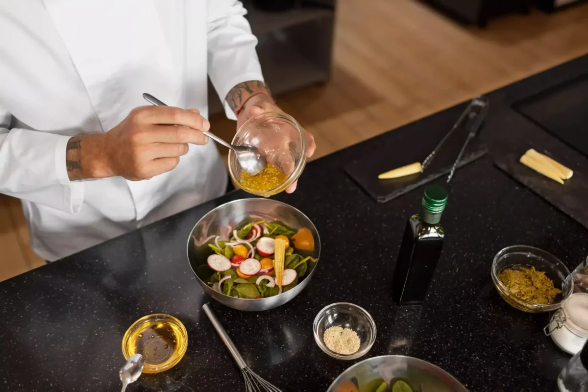 Professional chef preparing a fresh salad with homemade dressing in a modern kitchen.