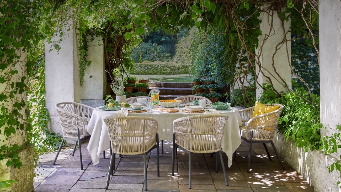 Shaded Mediterranean pergola with climbing greenery and an elegant outdoor dining table, showcasing climate-responsive architecture that blends nature and refined outdoor living.