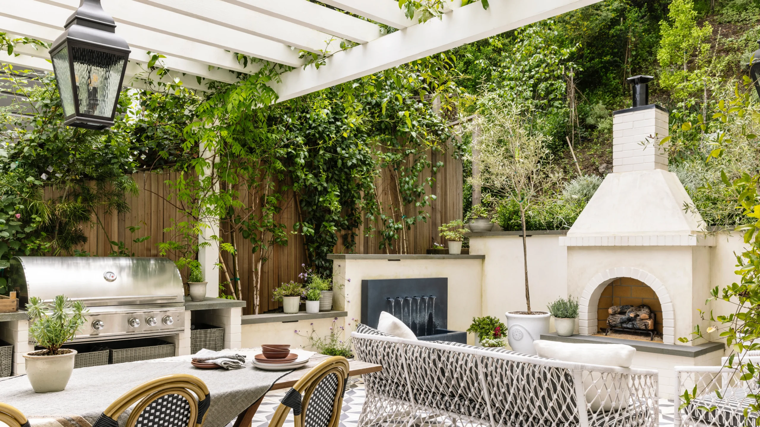 Elegant Marbella outdoor space featuring a pergola-covered outdoor kitchen with built-in grill, fireplace, and luxury outdoor furniture designed for long Mediterranean evenings.
