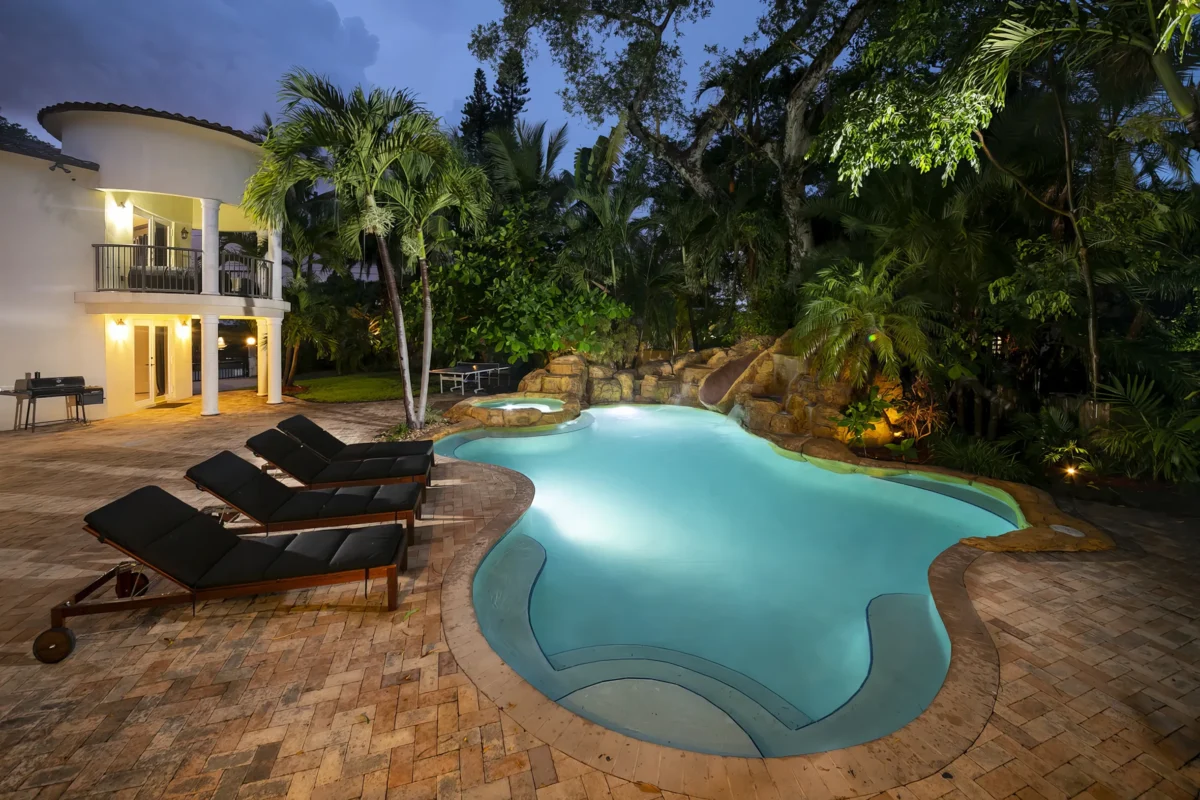 Luxury outdoor pool area in a Miami high-end villa featuring tropical landscaping, poolside loungers, and evening ambient lighting
