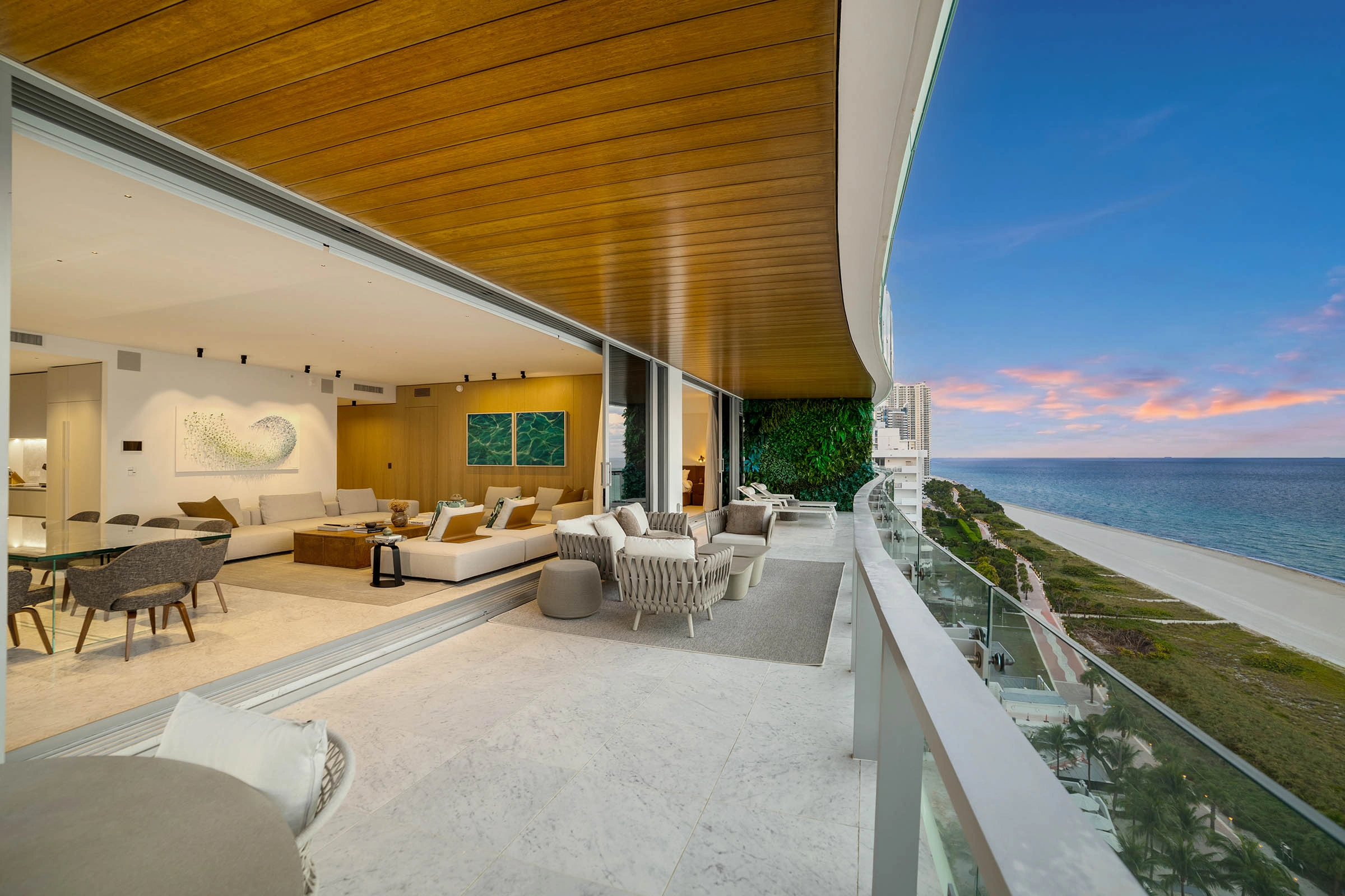 Luxury Miami oceanfront terrace featuring seamless indoor–outdoor living, with contemporary outdoor lounge furniture, warm wood ceilings, and panoramic Atlantic views at sunset.