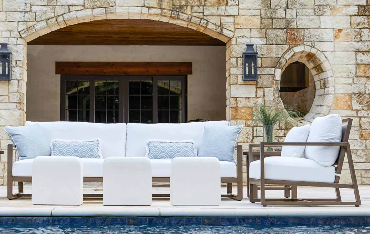 Refined poolside seating arrangement in a stone-clad coastal residence, showcasing minimalist luxury outdoor furniture designed for durability and elegance in a warm climate.