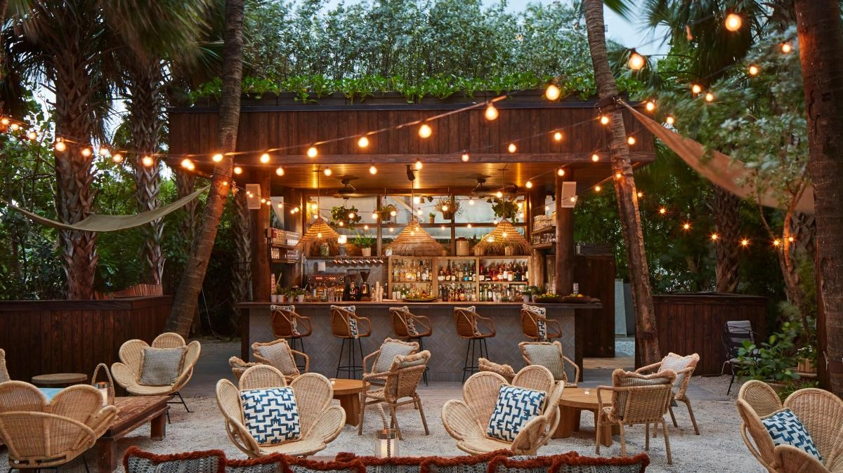 Atmospheric outdoor bar surrounded by palm trees, featuring natural materials and relaxed seating that reflect Miami’s tropical lifestyle and resort-inspired outdoor design.