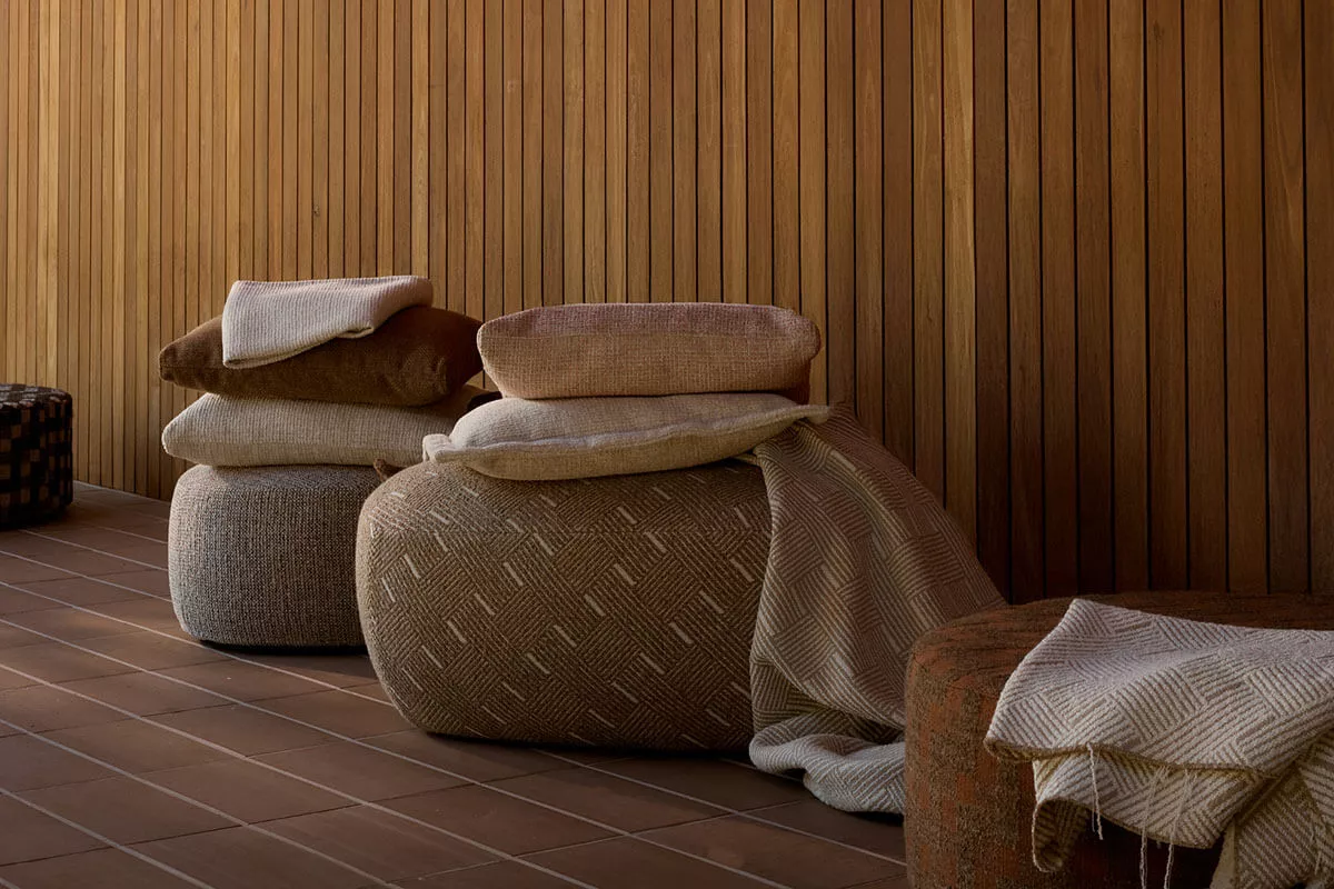 Textured outdoor poufs upholstered in weather-resistant fabric, styled against a wooden wall, highlighting tactile materials used in luxury outdoor furniture design.