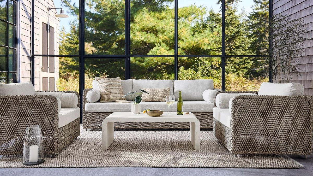 Luxury outdoor seating with woven sofas and neutral cushions in a serene indoor-outdoor living space surrounded by greenery.