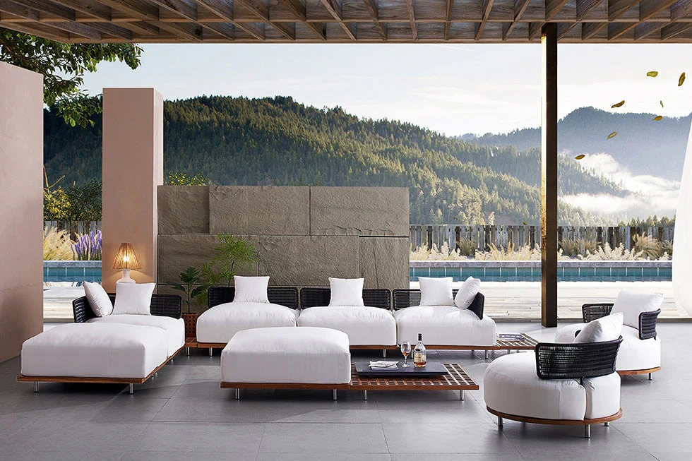 Luxury outdoor lounge design featuring modular outdoor seating with deep white cushions, set beneath a covered terrace overlooking a natural landscape, blending architectural structure with year-round comfort.