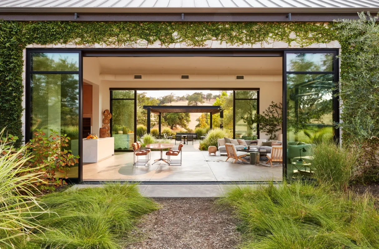 Contemporary indoor-outdoor living space with expansive sliding glass doors opening onto a refined outdoor lounge, where sculptural seating and landscaped surroundings create a seamless connection between architecture and nature.