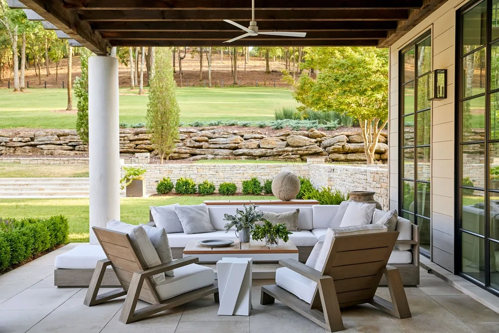 Cozy covered outdoor lounge with minimalist wooden outdoor seating, neutral cushions, and a low-profile table, designed for relaxed year-round use within a landscaped residential setting.