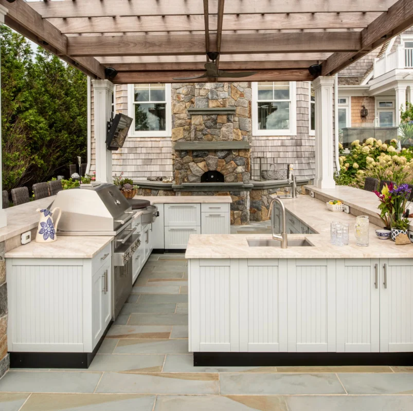Luxury outdoor kitchen with stone surfaces and wooden pergola, illustrating refined Mediterranean outdoor living and social cooking spaces.