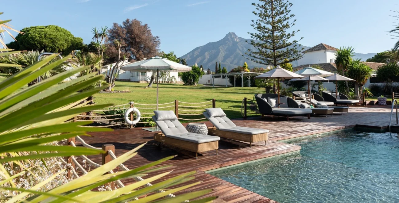 Elegant poolside lounge in Marbella with sun loungers, palm landscaping, and mountain views, embodying relaxed luxury outdoor living