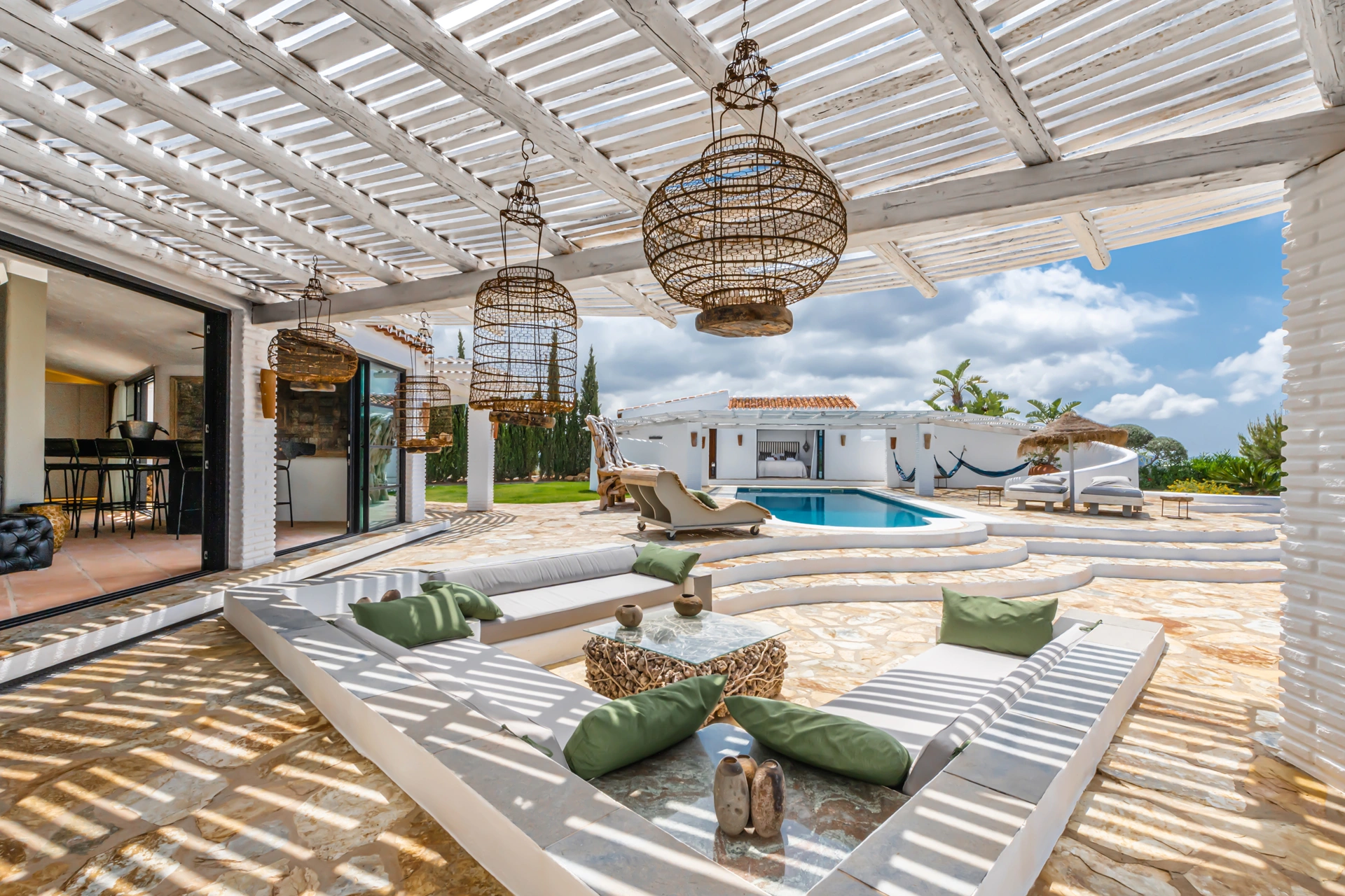 Mediterranean villa terrace in Marbella with pergola-shaded lounge, natural stone flooring, and seamless indoor-outdoor living design.