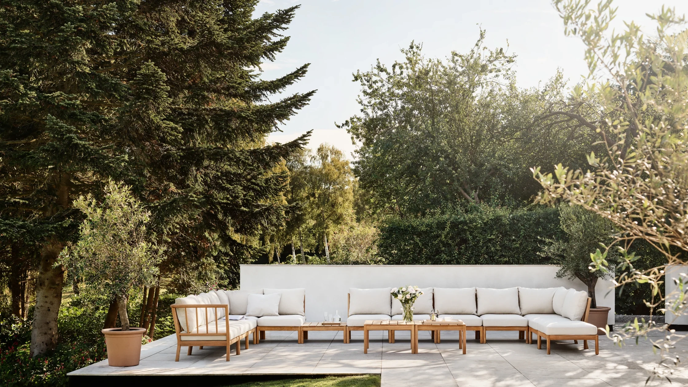 Modular outdoor sofa arranged on a minimalist garden terrace, featuring natural wood frames and light cushions in a serene luxury landscape.