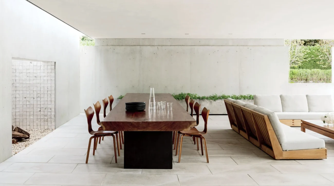 Minimalist luxury outdoor dining space with solid wood table and designer chairs under a modern architectural canopy.