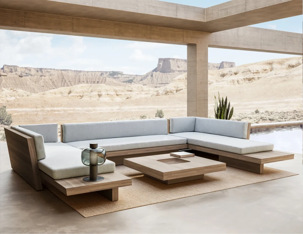 Contemporary outdoor design with luxury modular seating, natural wood furniture, and soft neutral textiles set within a modern architectural pavilion overlooking a desert landscape.