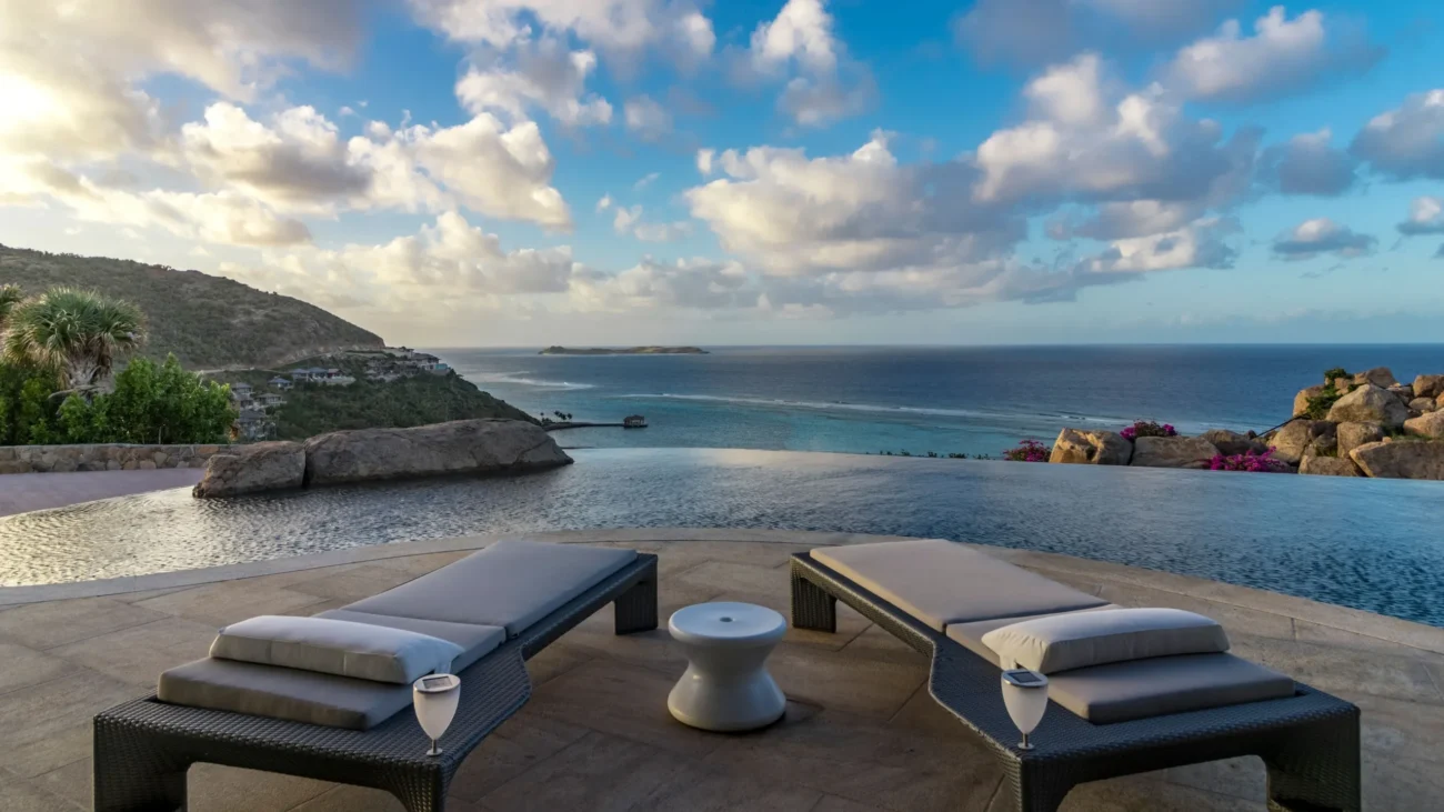 Luxury poolside furniture including teak poolside lounge chairs and upholstered daybeds arranged on refined terraces beside infinity pools, overlooking coastal and desert landscapes, designed for elegant outdoor living and resort-style comfort.