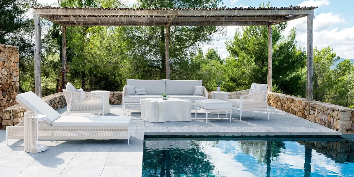 Luxury poolside furniture including teak poolside lounge chairs and upholstered daybeds arranged on refined terraces beside infinity pools, overlooking coastal and desert landscapes, designed for elegant outdoor living and resort-style comfort.