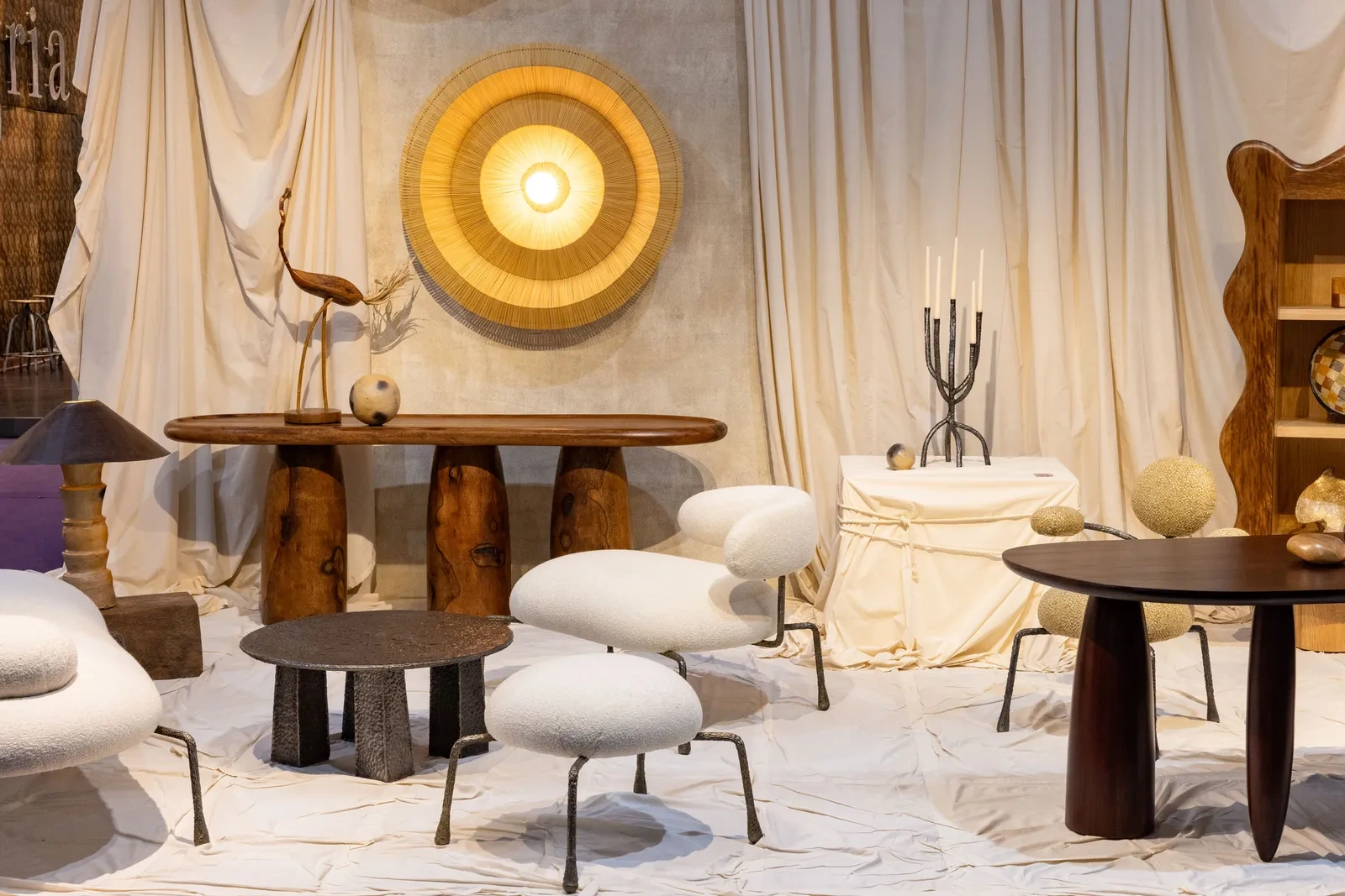Contemporary interior from Maison&Objet with cozy white chairs, rustic wooden tables, and textured beige drapes. A large woven wall light adds warmth and elegance.