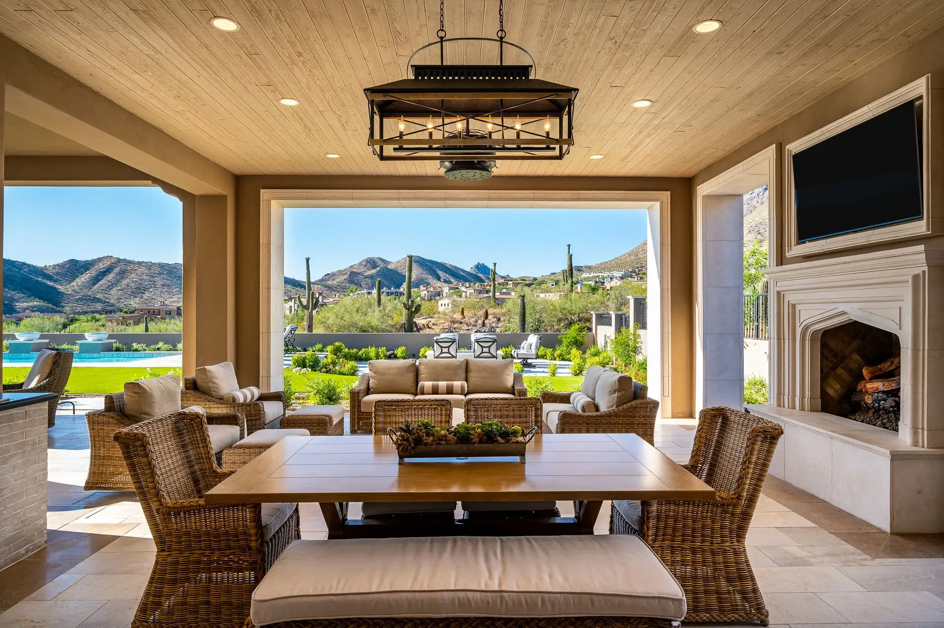 Luxurious patio with wicker furniture, a wooden dining table, and a fireplace. Large open doorway reveals a stunning mountain view, creating a serene ambiance, present in many luxury homes.