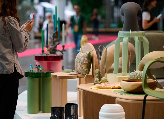 A person photographs an art display featuring eclectic sculptures and decorative objects in pastel shades. The setting is vibrant and creative.