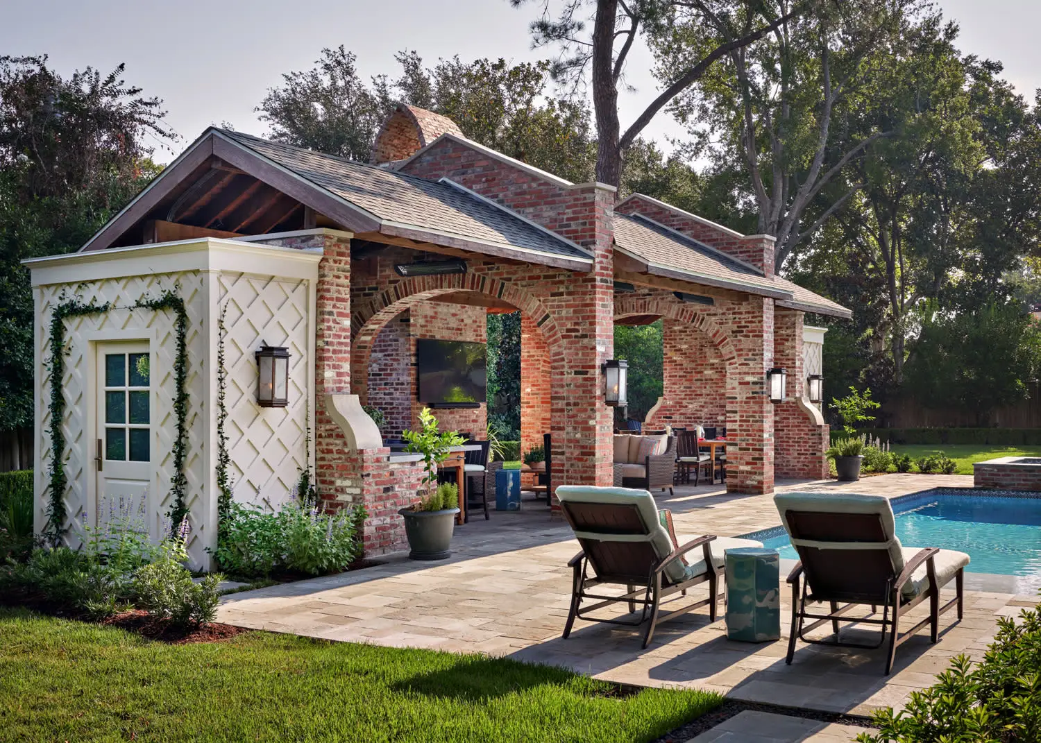 Charming outdoor space featuring a brick pavilion with arches, cozy seating, and a poolside view. Sunlit and tranquil atmosphere with lush greenery.