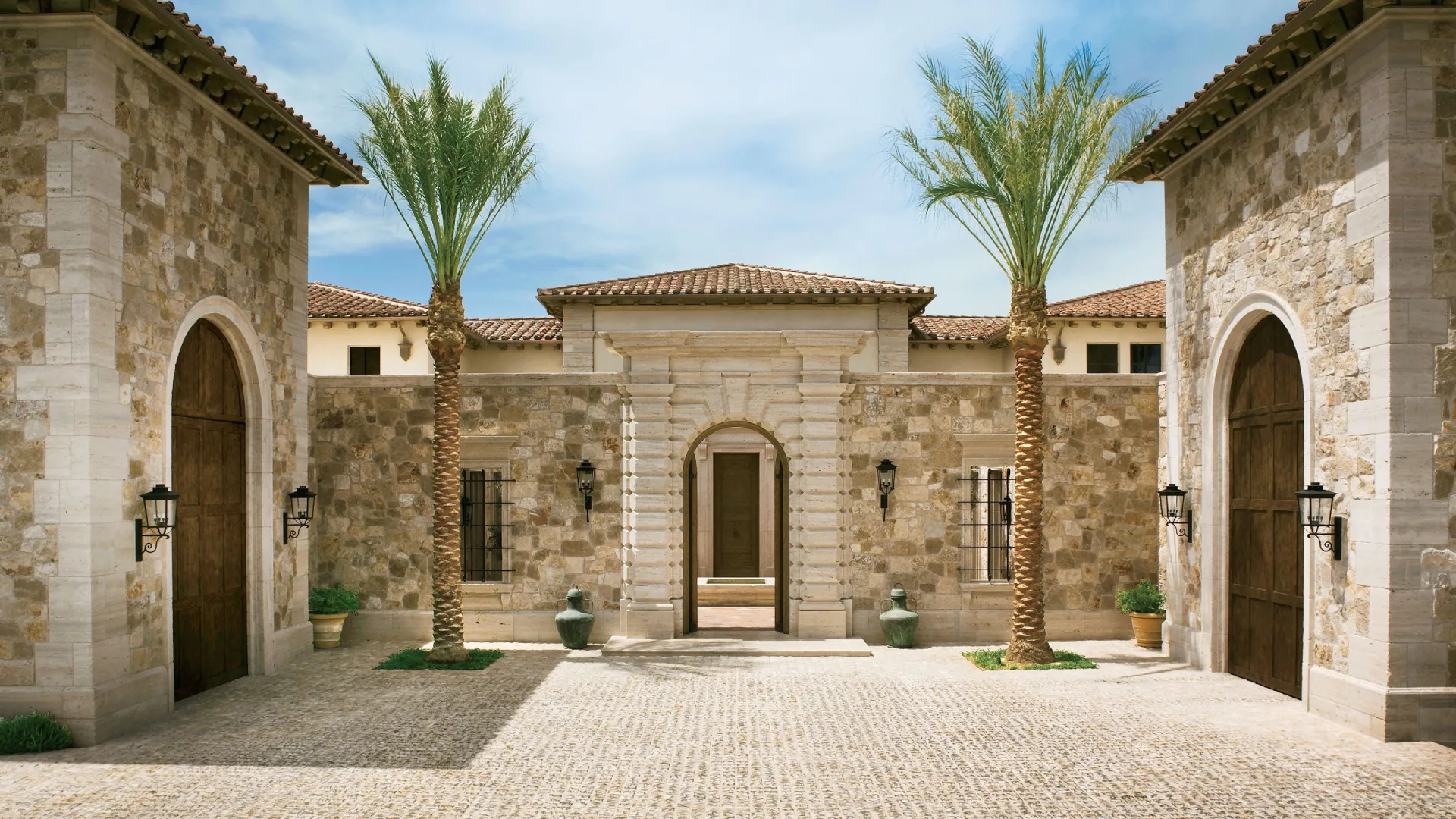 Historic Italian villa courtyard with stone arches, fountain, cypress trees and elegant Mediterranean outdoor living design.