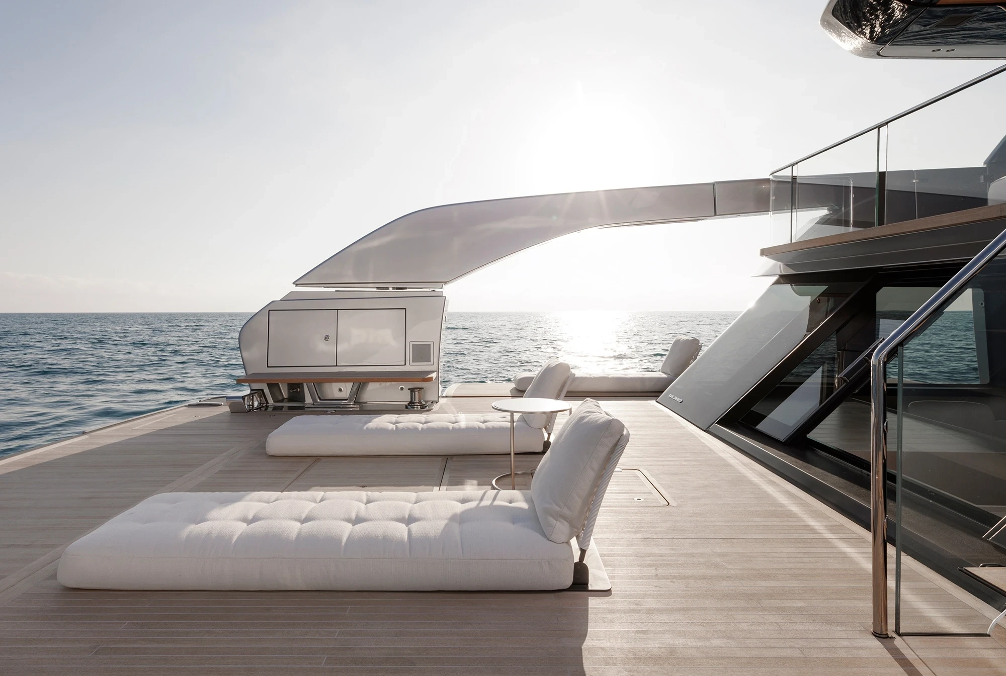 Luxurious yacht deck with plush white loungers facing the calm ocean. The sun is setting, casting a serene glow over the tranquil sea.
