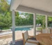Covered patio by designer Craig Reynolds with a pool surrounded by lush greenery and palm trees, offering a view of the ocean at sunset. Relaxing and serene atmosphere. with wooden table and chairs overlooking a serene pool surrounded by lush greenery and lounge chairs, evoking a relaxing ambiance.