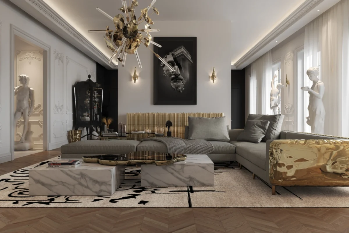 Luxurious living room with gold and white decor. Features gray sectional sofa, marble coffee tables, modern chandelier, large artwork, and classical sculptures.