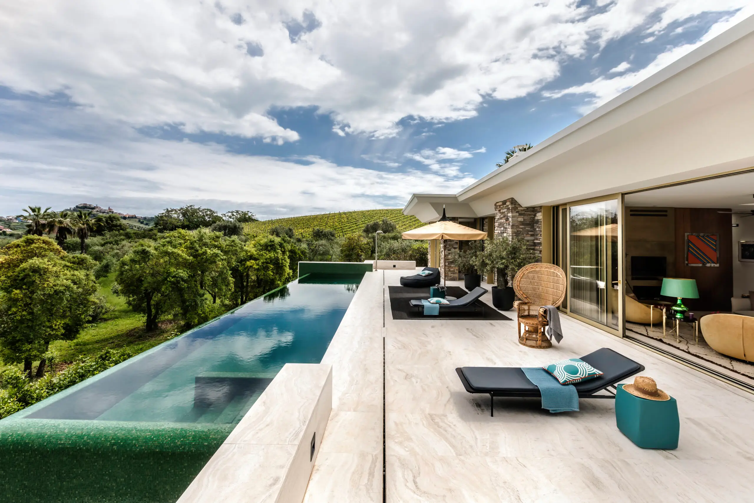 Outdoor luxury living design featuring a contemporary villa terrace with infinity pool, natural stone flooring, modern lounge furniture, and seamless indoor-outdoor architectural flow.