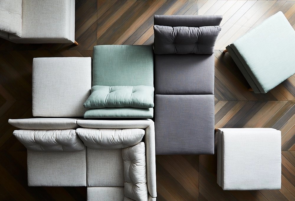 Top view of modular sofas and an ottoman arranged on a wooden herringbone floor. Fabrics in soft gray, teal, and white create a modern, cozy ambiance.