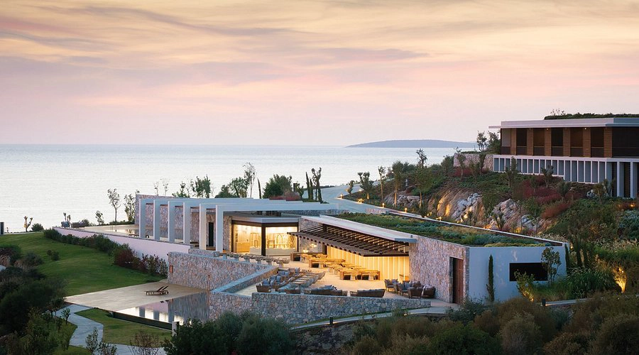 Modern cliffside resort at sunset, overlooking the sea. The building blends with lush greenery, warm lighting, and a serene, tranquil atmosphere.