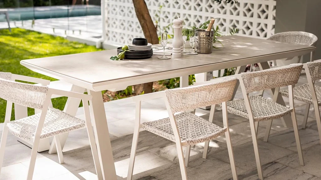 Modern outdoor patio set with a long white table and woven chairs, set for dining, highlighting properly maintained luxury outdoor furniture.