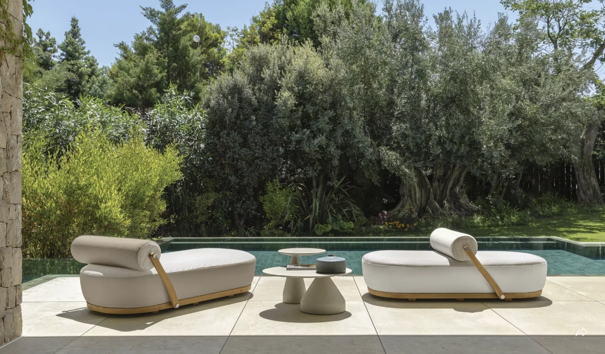 Poolside scene with two plush, white loungers facing a pool, surrounded by lush greenery. Calm, inviting ambiance with natural tones.